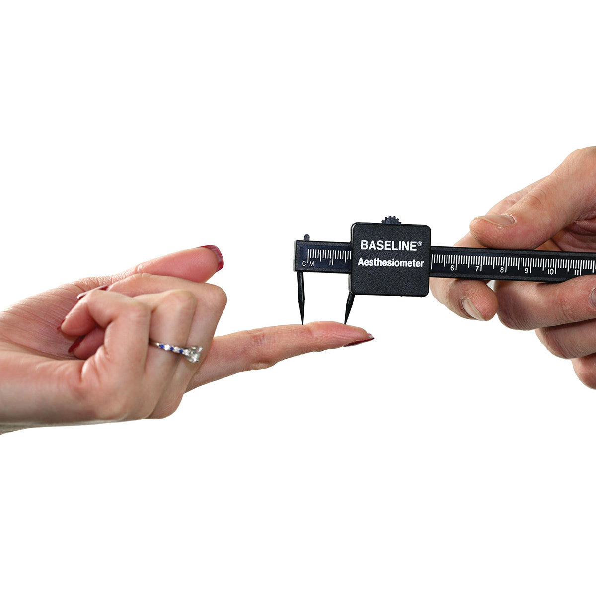 Two hands use a Baseline Aesthesiometer to test sensation on a finger, with a black scale and pointed tips.