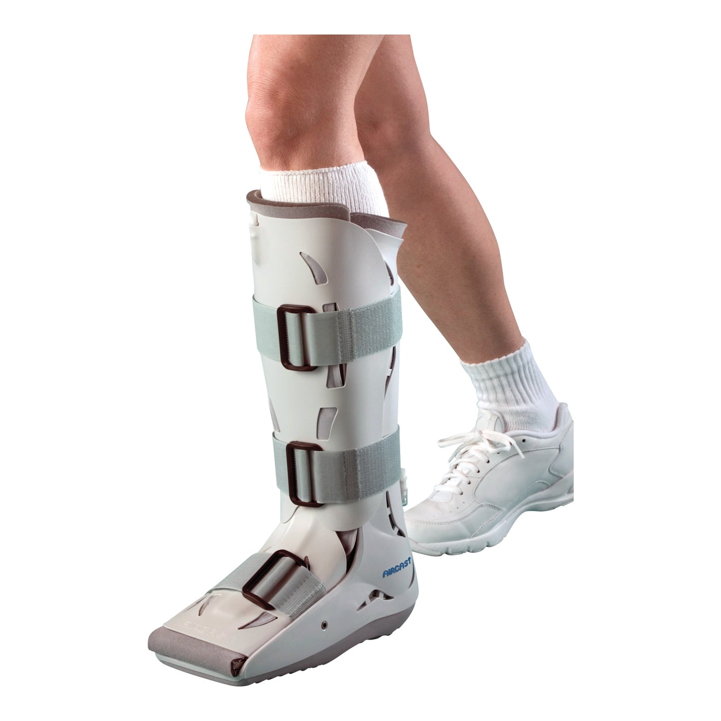 A person wearing an Aircast Pediatric XP Walker boot on the left leg, secured with three straps, next to a white sneaker.