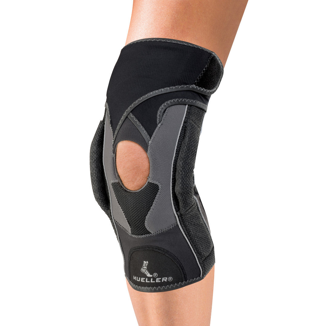 A person wearing a Mueller Hg80 Premium Hinged Knee Brace with a cutout at the knee and a supportive black and gray design.