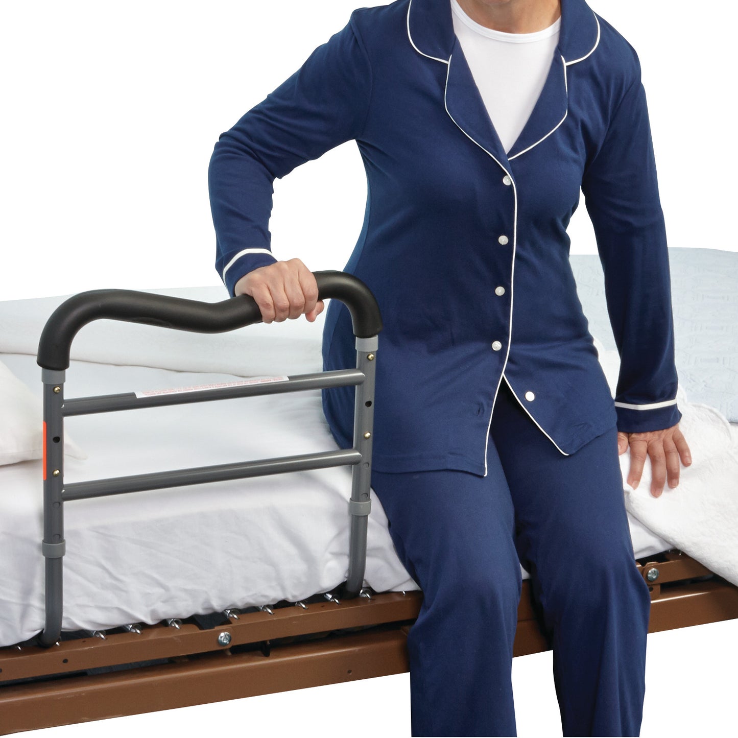 A person in blue pajamas uses the AliMed AliRail Bed Rail, attached to the side of a bed, for support while sitting up.