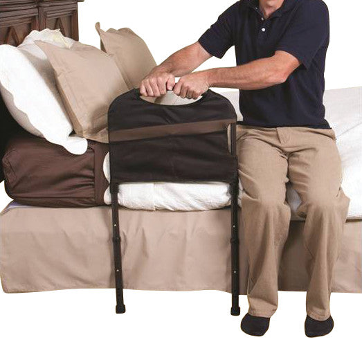 A person is using a Stander Stable Rail attached to a bed, providing support for sitting or standing.