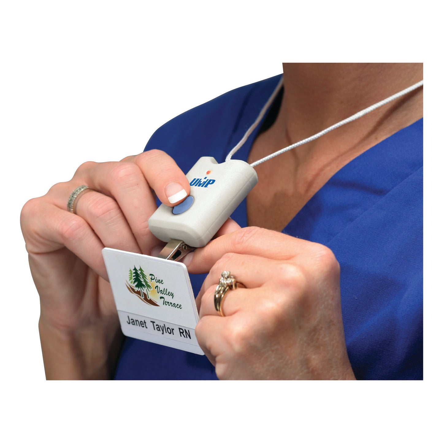 A person wearing a blue uniform uses the UMP Deluxe Bed Sentry Alarm, holding it near an ID badge on a retractable cord.