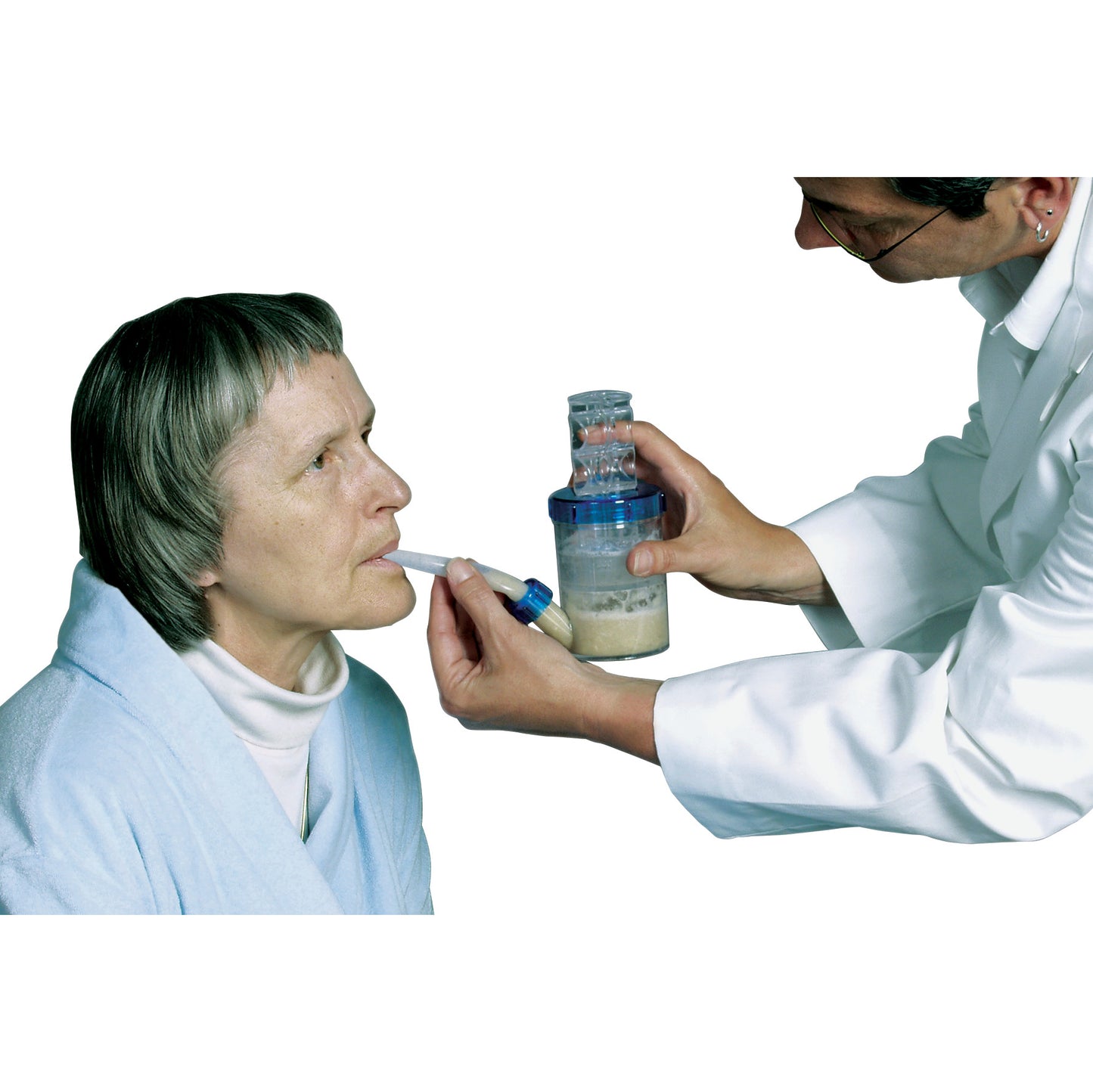 An older woman in a blue robe uses the AliMed Feeding Assistant with a straw. A person holds the assistive feeding device.