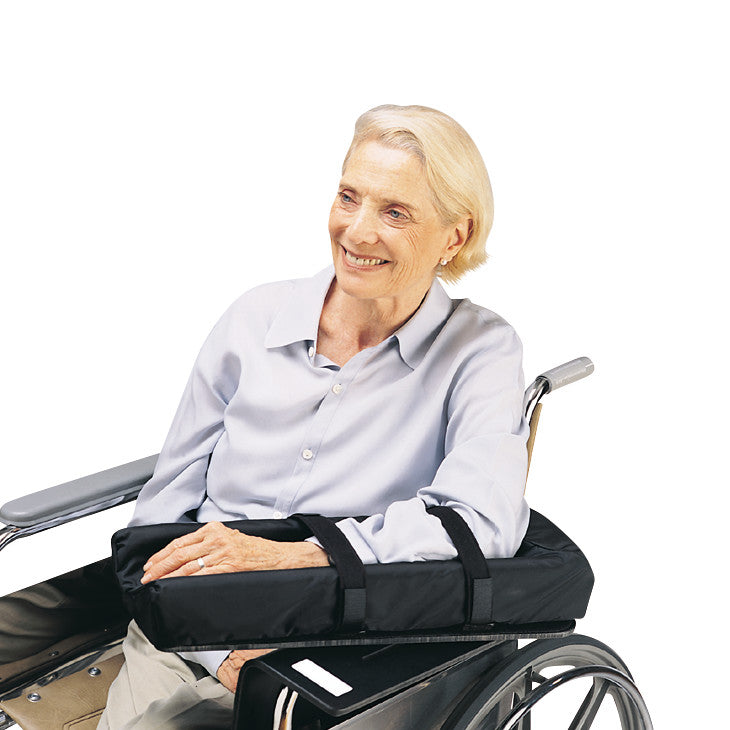 An older adult in a wheelchair uses the SkiL-Care Level Wheelchair Mobile Arm Support, resting her arm on the cushioned accessory.