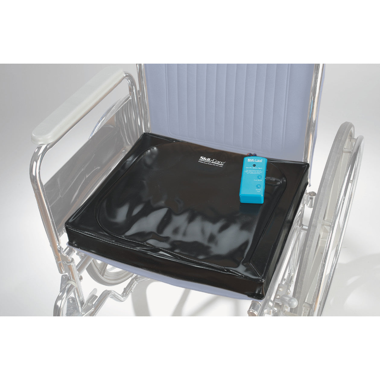 A wheelchair with a SkiL-Care Gel-Foam Pad Alarm on the seat, featuring a black cushion and a blue alarm device.
