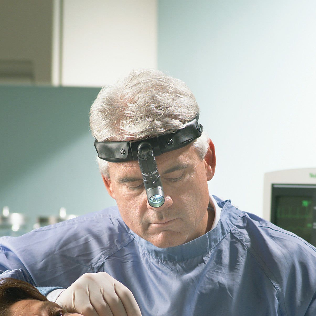 A medical professional wearing a Welch Allyn Green Series Procedure Headlight focuses on a procedure with a patient in a clinical setting.
