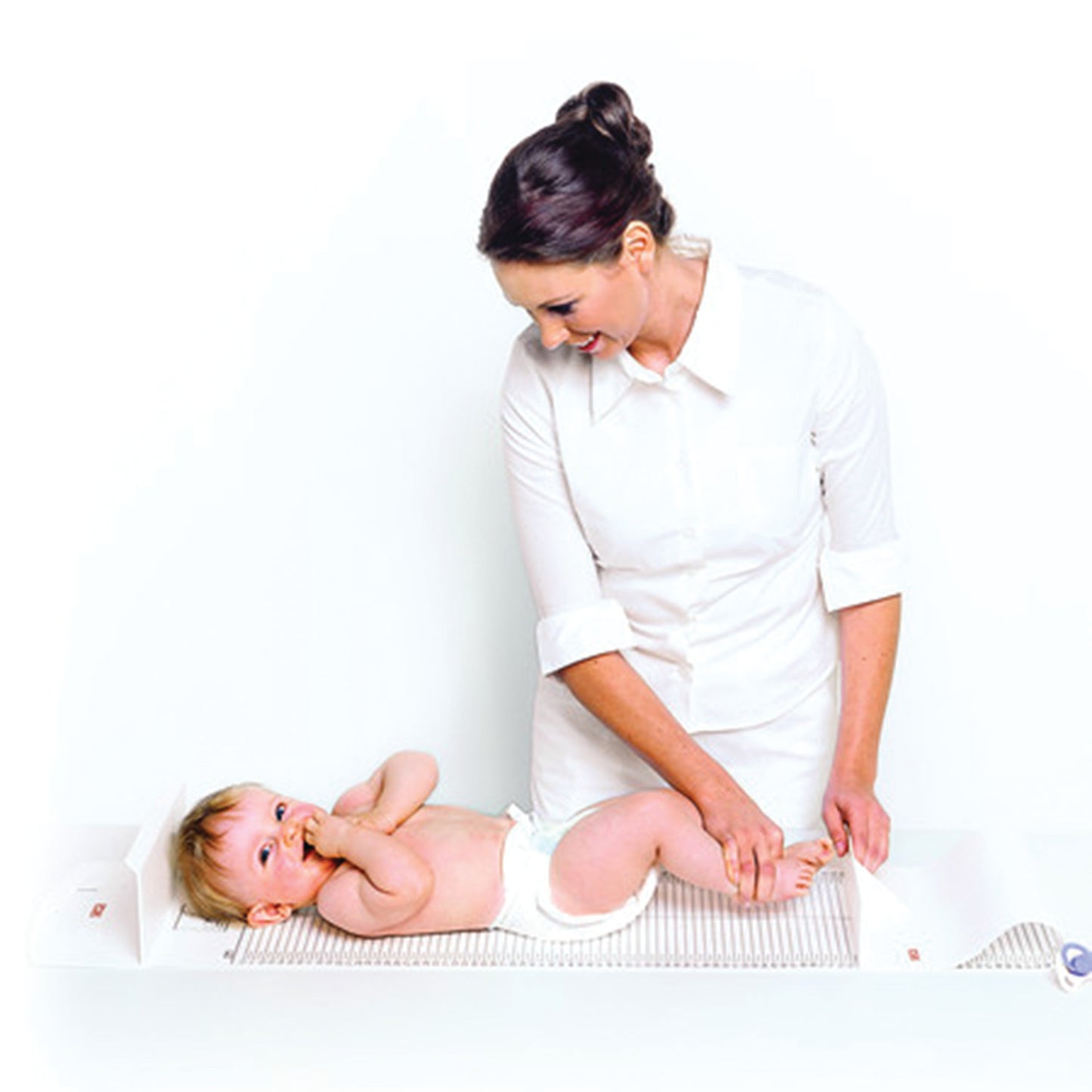 A woman measures a baby on a white Seca 210 Mobile Measuring Mat. The baby is lying on the mat, wearing a diaper.