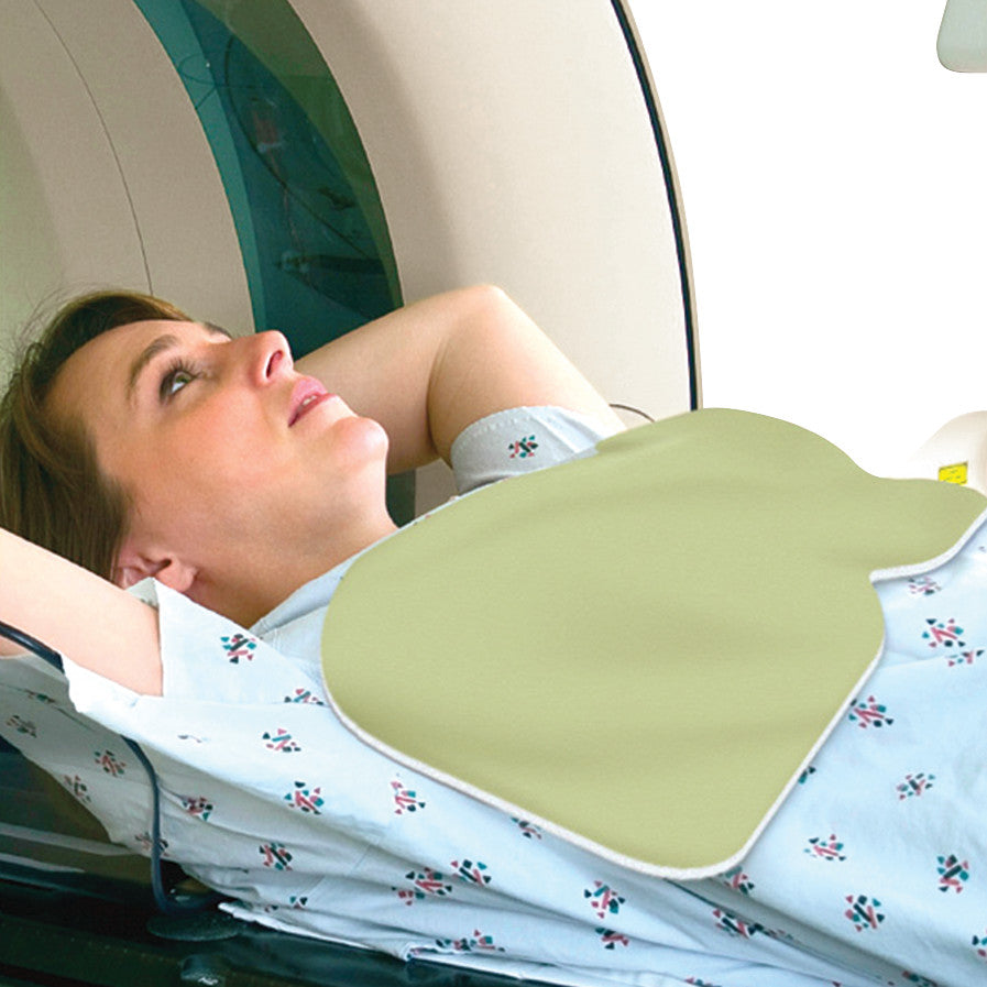 A woman in a hospital gown lies inside a CT scanner, with a SecureShield CT Breast Shield placed on her chest.