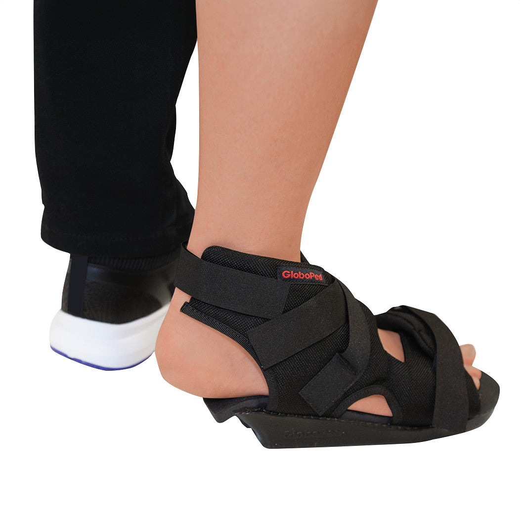 A person wears a Bauerfeind GloboPed Heel Relief Orthosis on one foot and a regular shoe on the other.