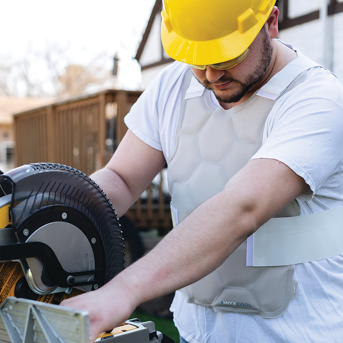 A person wearing a yellow hard hat and the Xena Therapies Onyx Cool Safety Pro Vest operates a circular saw outdoors.