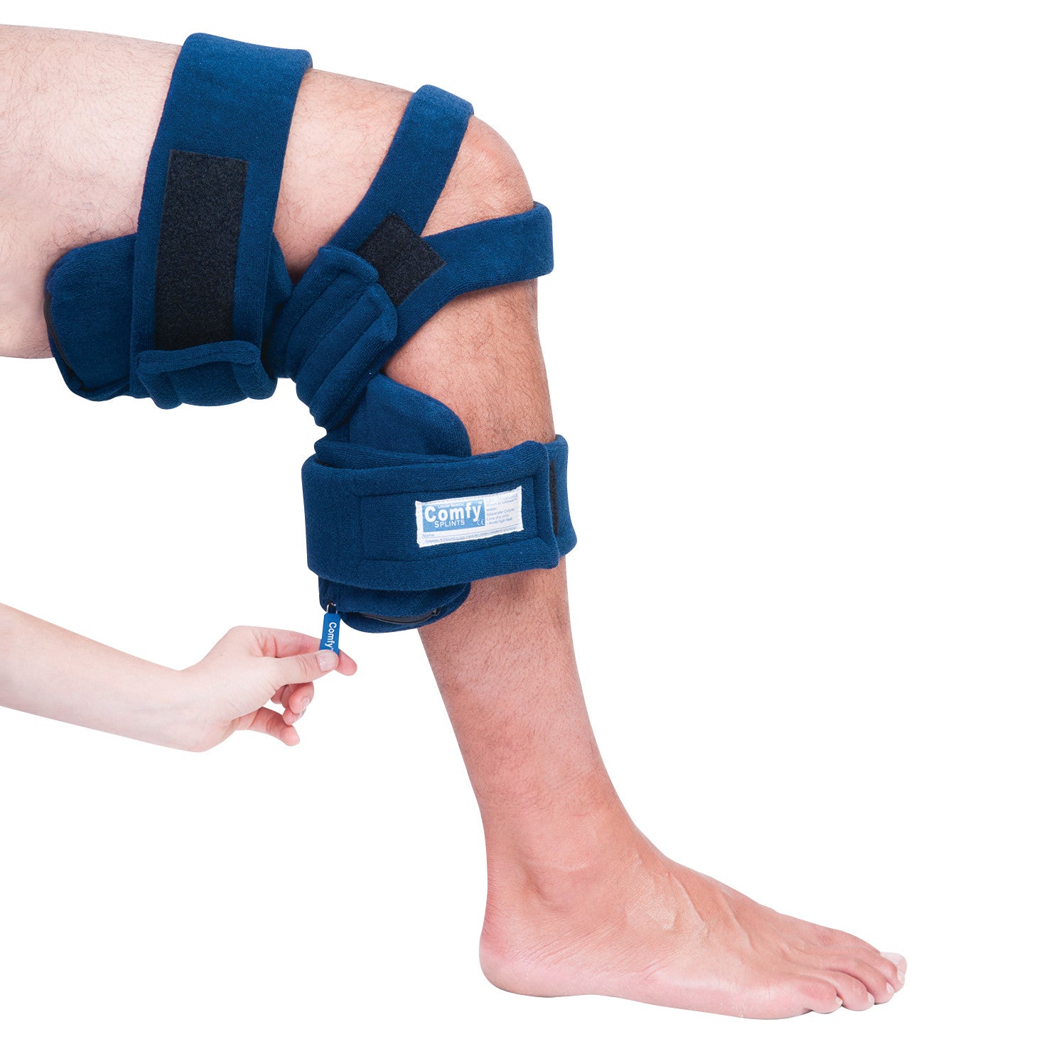 A person's leg wearing a Comfy Splints Adult Locking Knee Orthosis, secured with straps, while a hand adjusts it.