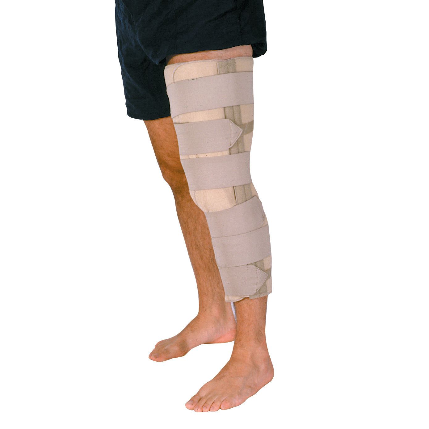 An individual wearing a Foam Knee Immobilizer secured with beige straps, standing barefoot in black shorts.