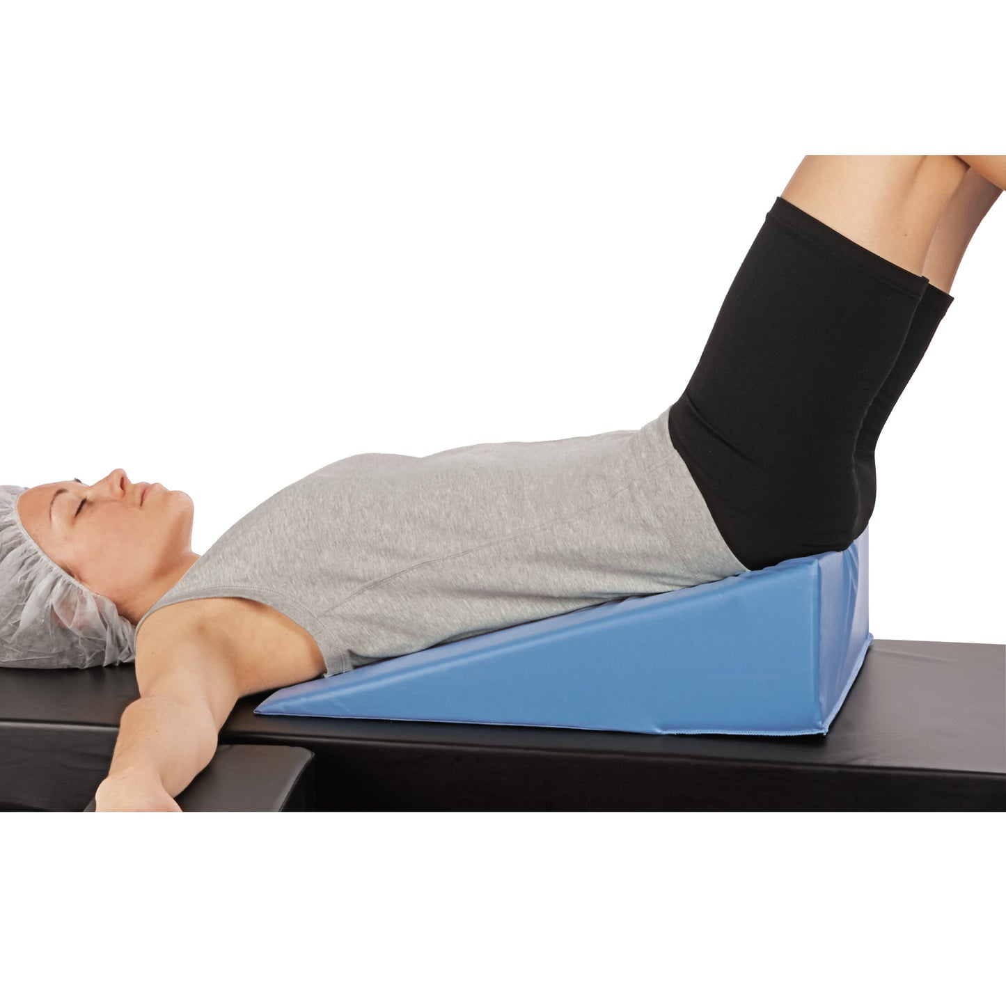 A person reclines on the AliMed Perineal/Endovaginal Wedge. They're on a blue foam wedge with legs elevated, wearing a gray shirt.