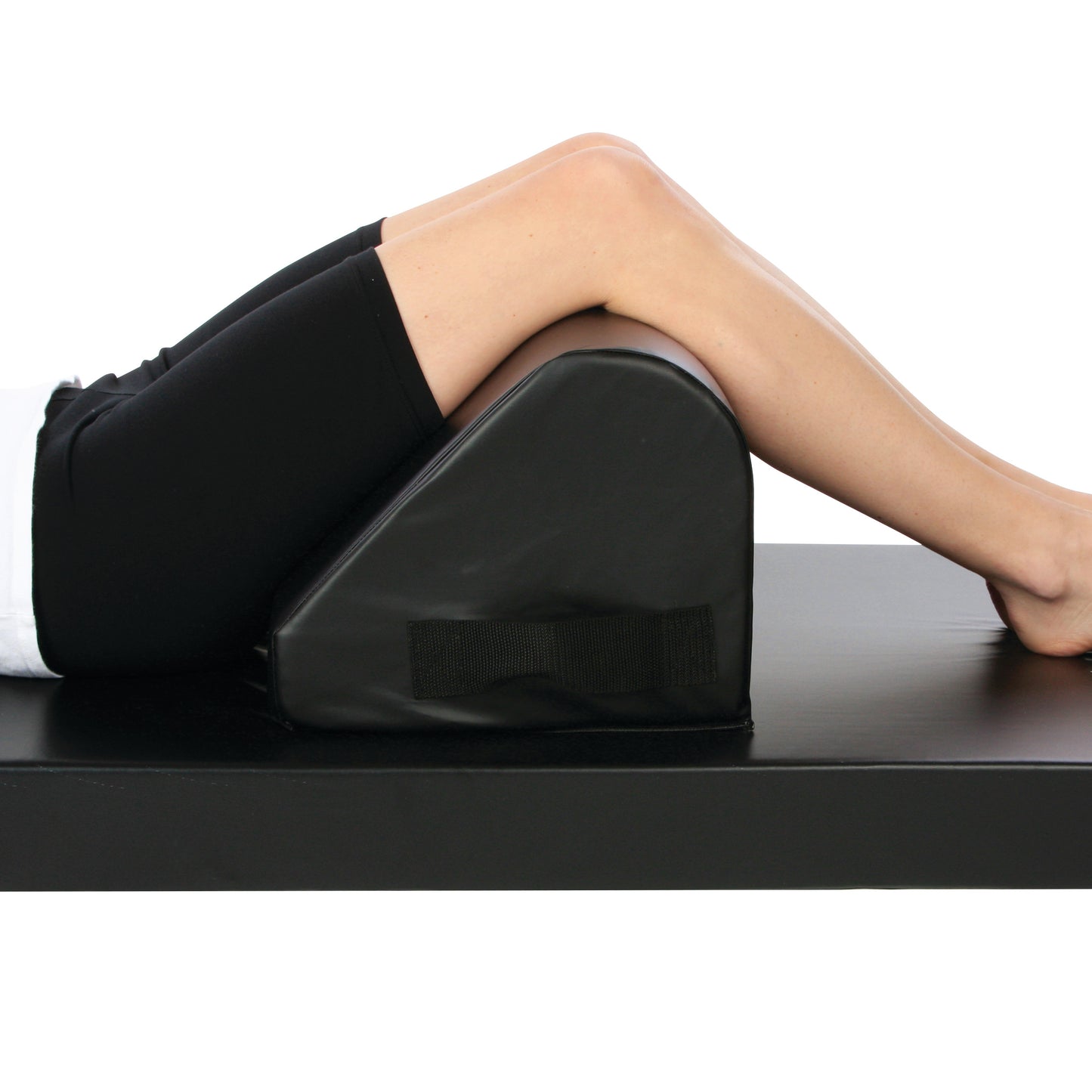 A person rests their legs over the AliMed Vinyl-Covered Tall Knee Bolster, a black wedge-shaped cushion on a flat surface.