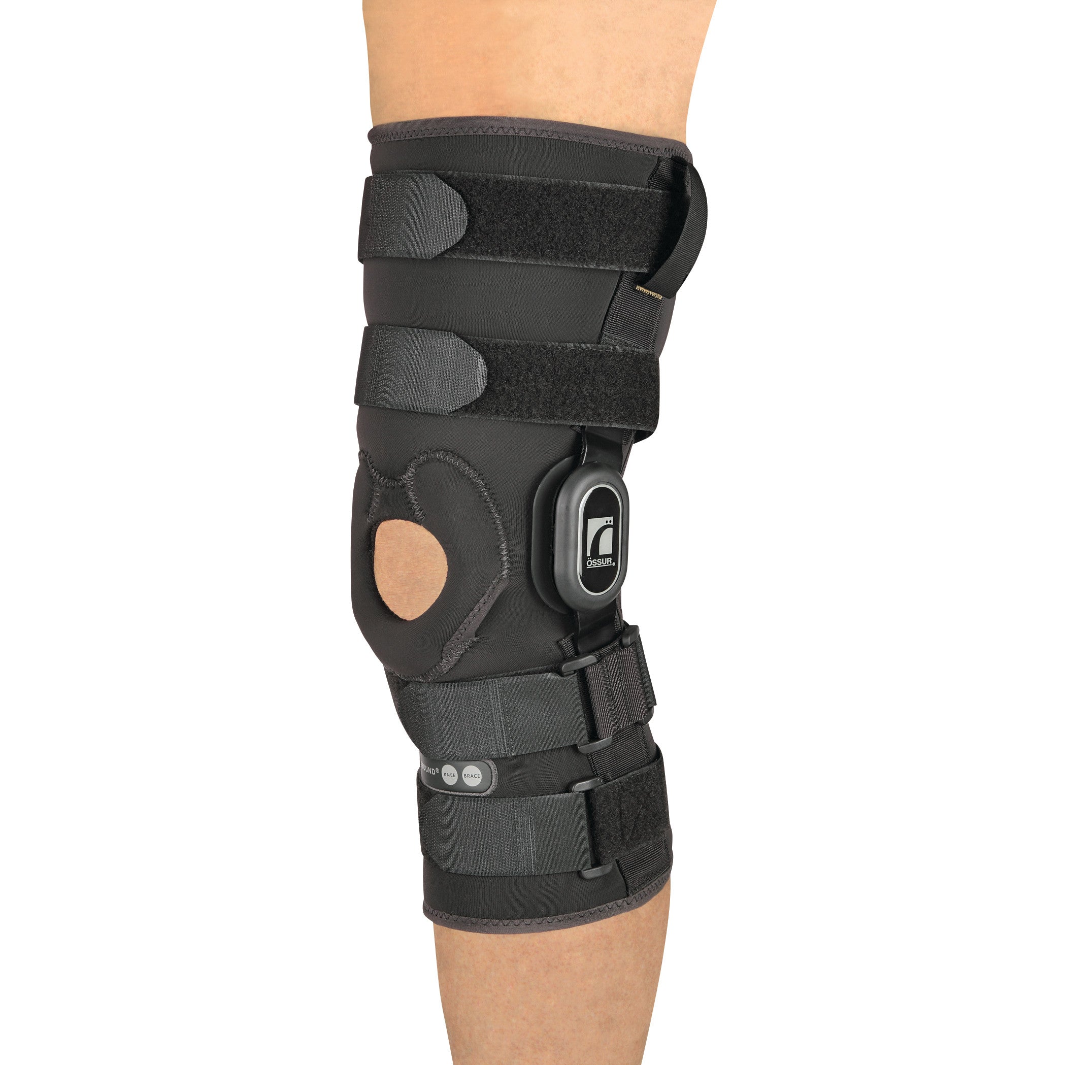 A person wears an Ossur Rebound ROM Knee Brace with Long Sleeve, featuring adjustable straps and a circular cutout over the kneecap.