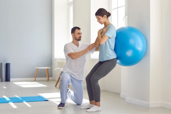 physical therapist helping patient with therapeutic ball wall exercise