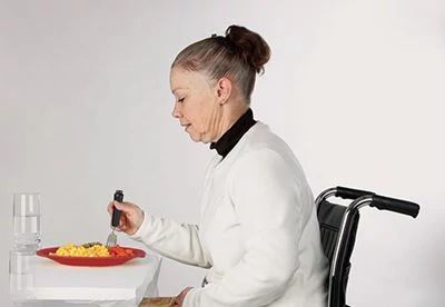 woman sitting in wheelchair eating using assitive dining aids