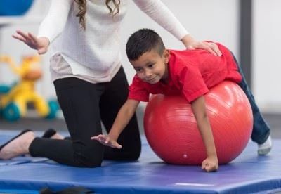 physical therapist helping pediatric patient on exercise ball