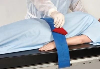 nurse putting patient safety strap on patient on operating table