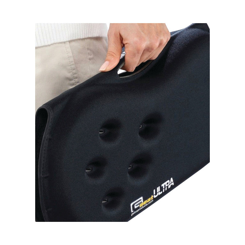 A person holds a black Gelco GSeat Ultra Portable Gel Seat, featuring a handle and indented surface texture.