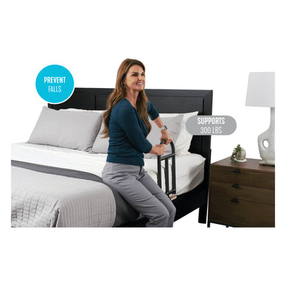 A woman uses the Stander BedCane for support while sitting on a bed. Text states it prevents falls and supports up to 300 lbs.