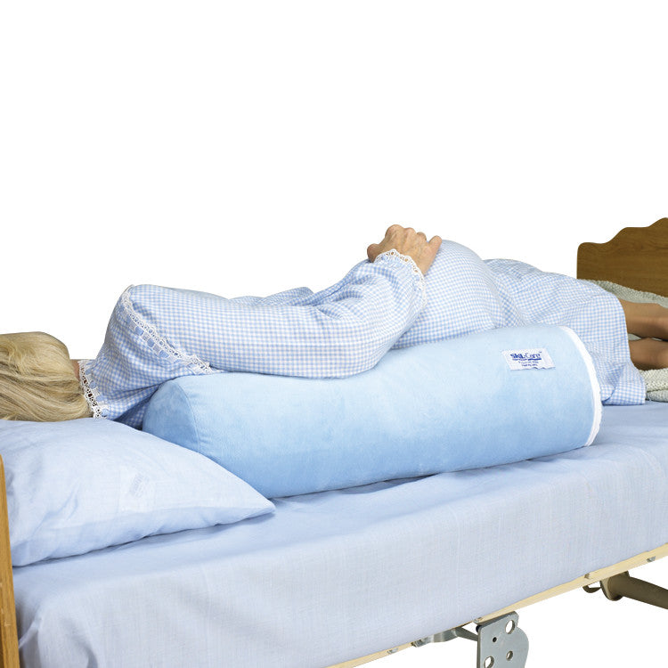 A person lies on a bed using the SkiL-Care Ultra-Soft Bed Bolster, a blue, cylindrical cushion, for side support.
