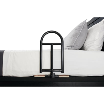 A Stander BedCane attached to the side of a bed with white sheets and gray pillows, providing support for a person getting in and out.