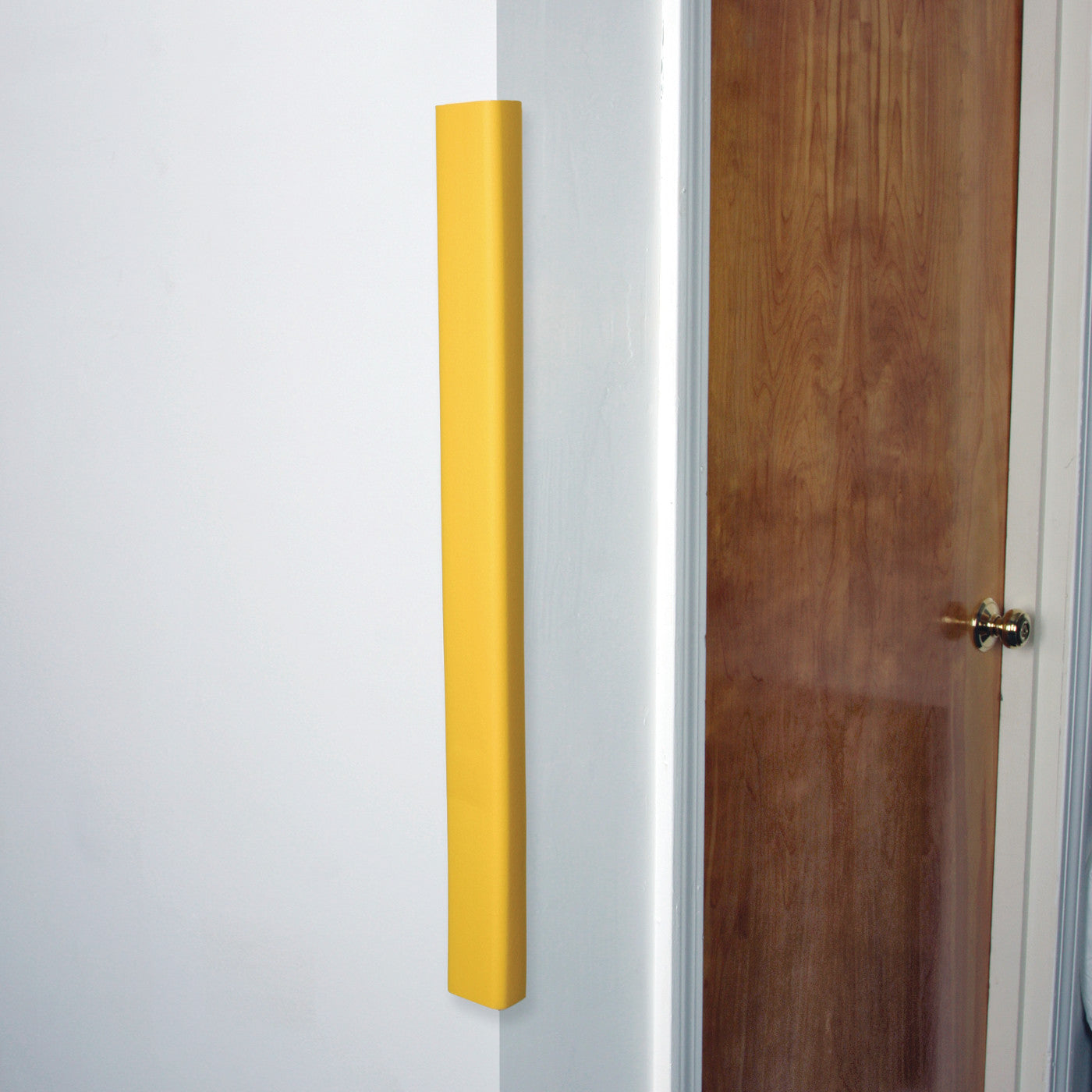 AliMed SoftEdge Edge Protector in bright yellow, attached to the corner of a white wall next to a wooden door with a silver knob.