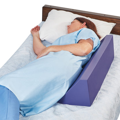A person lies on their side in bed with an AliMed Tuff-Coat Wedge Positioner, a purple triangular cushion, supporting their back.