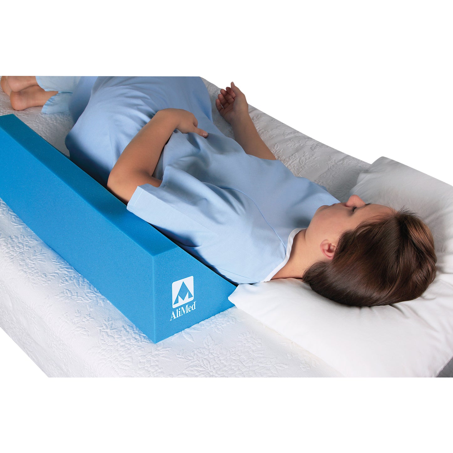 A person on a bed uses the AliMed Uncovered Body Positioning Wedge for support on their side. The wedge is blue and rectangular.