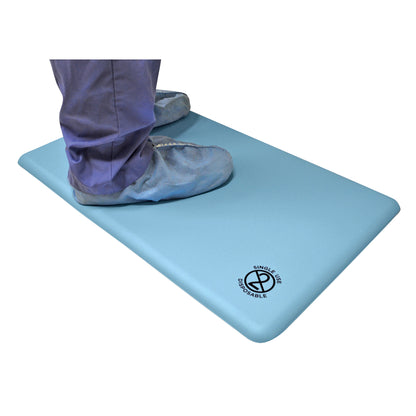 Person standing on a GelPro Disposable Surgical Comfort Floor Mat. The mat is blue with a 'Single Use Disposable' label.