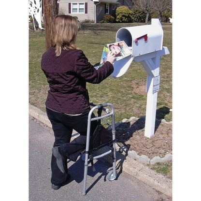 A woman with a walker retrieves mail using the SafetySure The Knee Sling, supporting her injured leg, near a white mailbox.