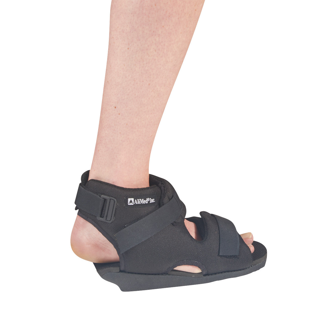 A person wearing an AliMed Open Heel Orthosis, a black orthopedic shoe, with adjustable straps, designed for foot support.