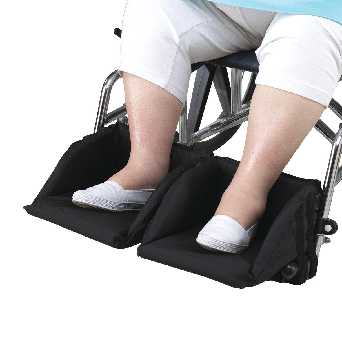 A person in a wheelchair uses SkiL-Care Swing-Away Foot Supports. The supports are black, cushioning the feet with white shoes.