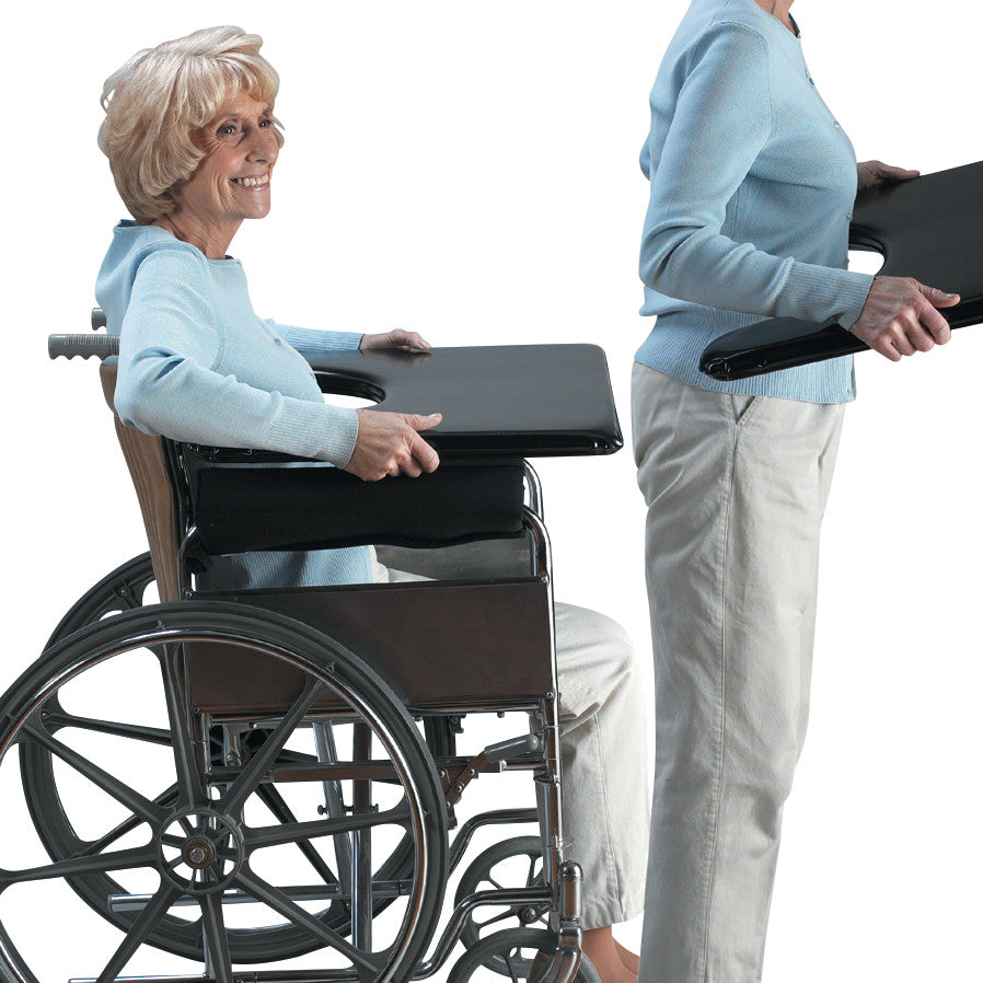 A person uses the SkiL-Care Lift-Away Lap Tray on a wheelchair. Another person is standing, holding the tray.