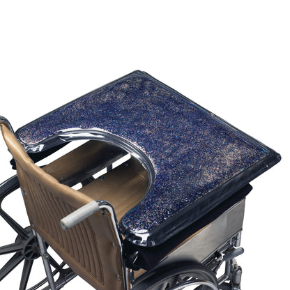 A wheelchair features the SkiL-Care Lift-Away Gel-Top Sensory Stimulation Tray with a glittery, blue gel surface for sensory stimulation.