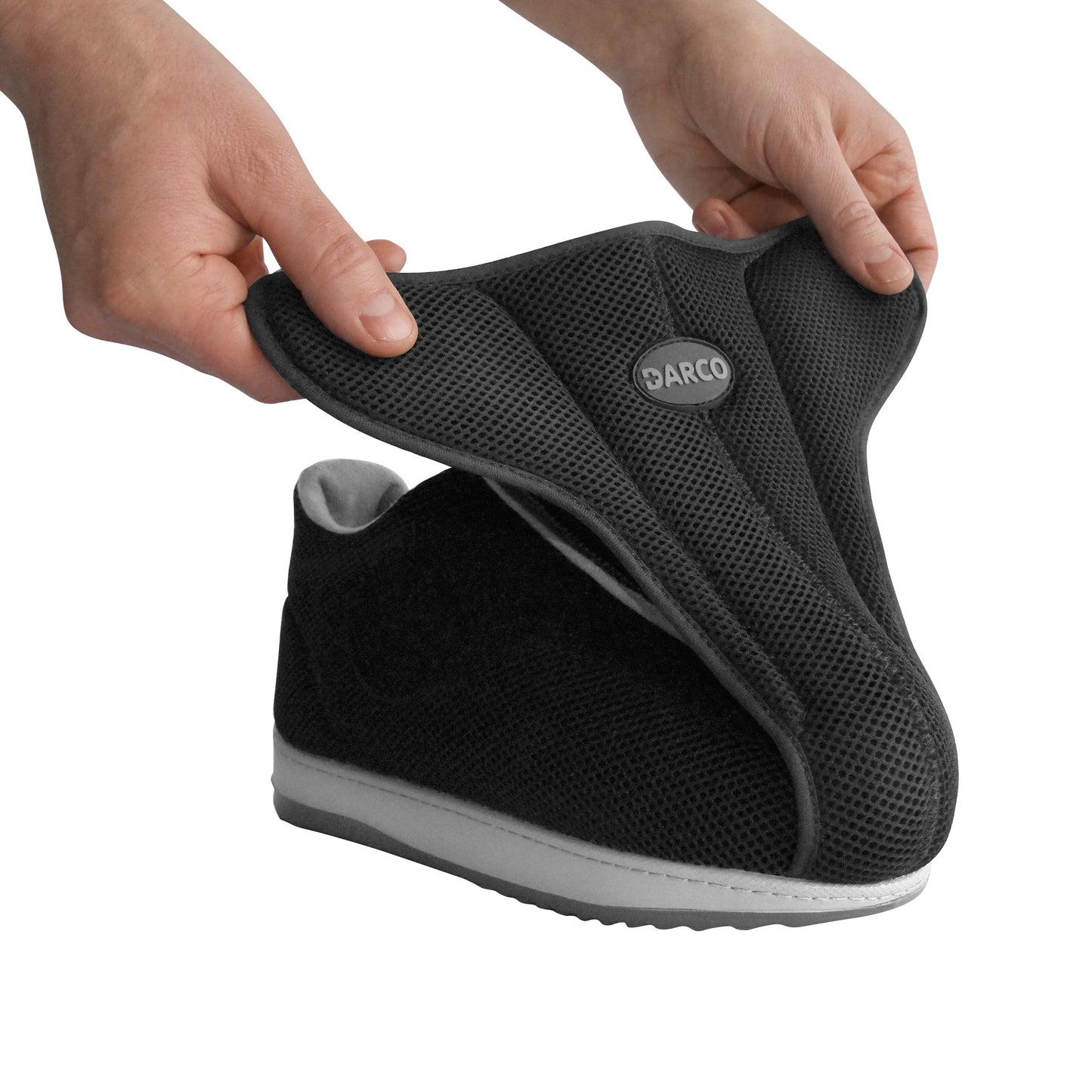 Hands opening the DARCO AllRound Shoe with a textured black mesh wrap, revealing the wide opening and soft interior for easy foot access.