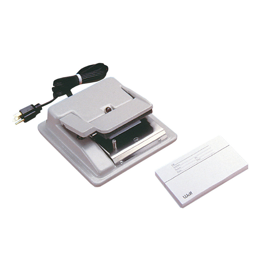 A Wolf ID Printer with an electrical plug is shown next to a stack of name cards, featuring a flat printing platform and a cord.