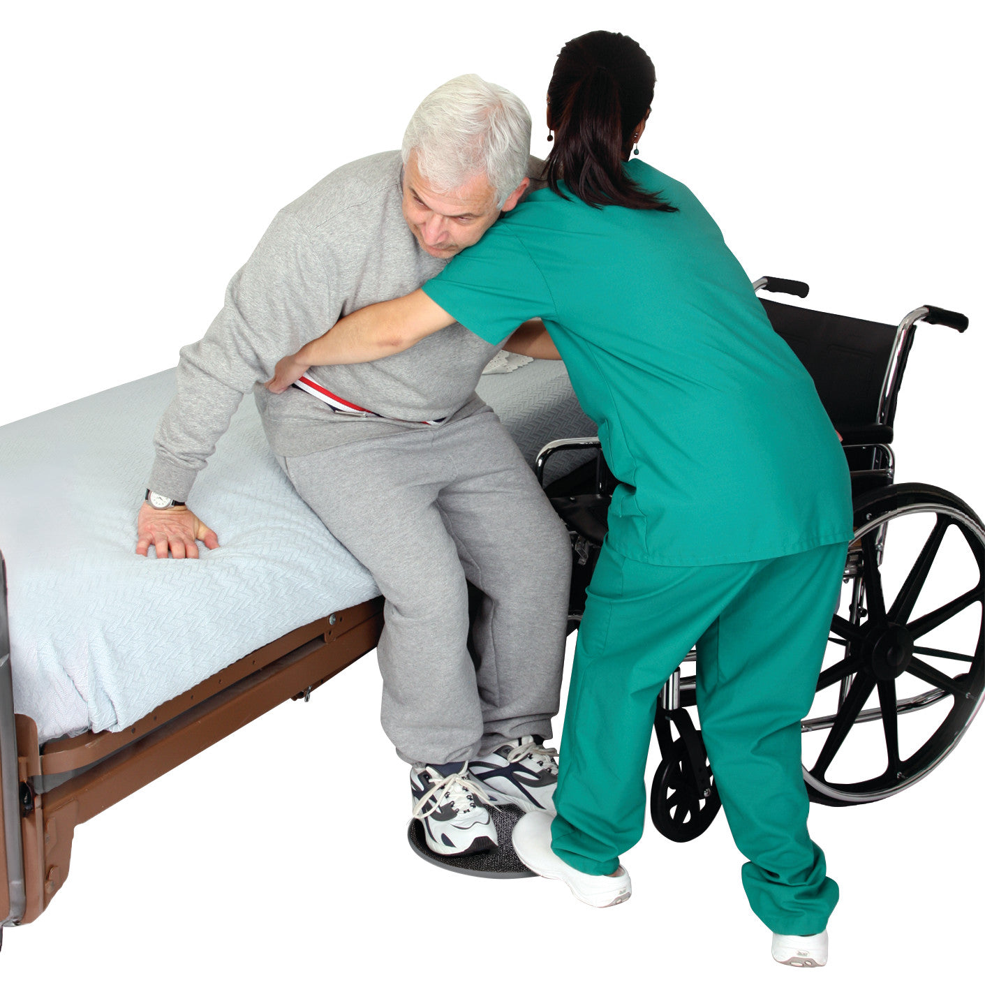 A caregiver assists an elderly man from a bed to a wheelchair using a SafetySure Pivot Disc under his feet.