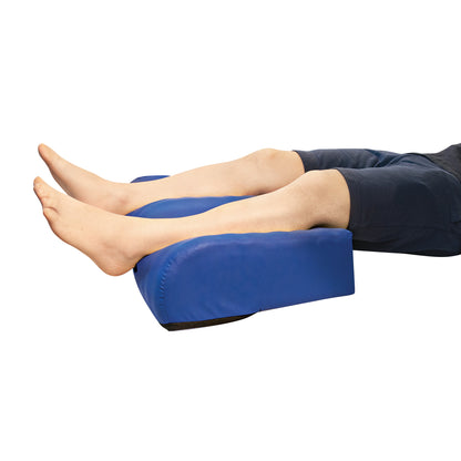 Person's legs rest on the NYOrtho ZERO-G Heel Pillow ULTRA, a blue cushion designed to elevate and support the heels.
