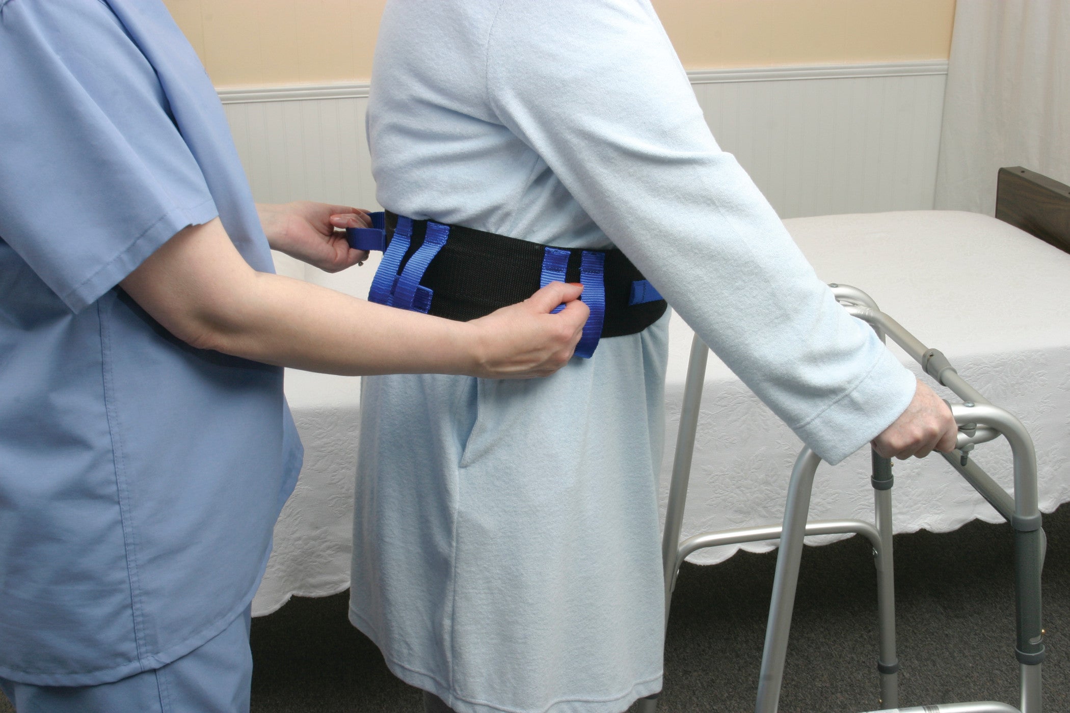 A nurse assists a person wearing an AliMed Ambulation Belt. The individual also uses a walker for support.