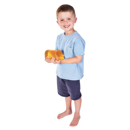 A young boy holds an AliMed AliGel Chest Roll. He is wearing a light blue shirt and dark shorts, standing barefoot.