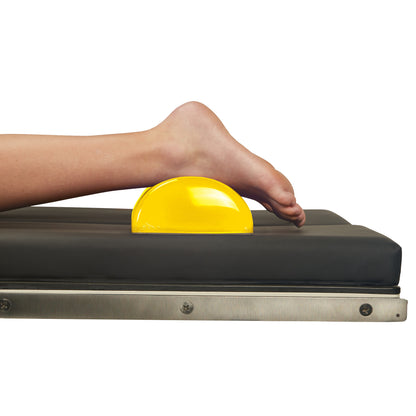 A leg is positioned on an AliMed AliLite Dome Positioner, a yellow foam support on a black padded surface, helping elevate the limb.