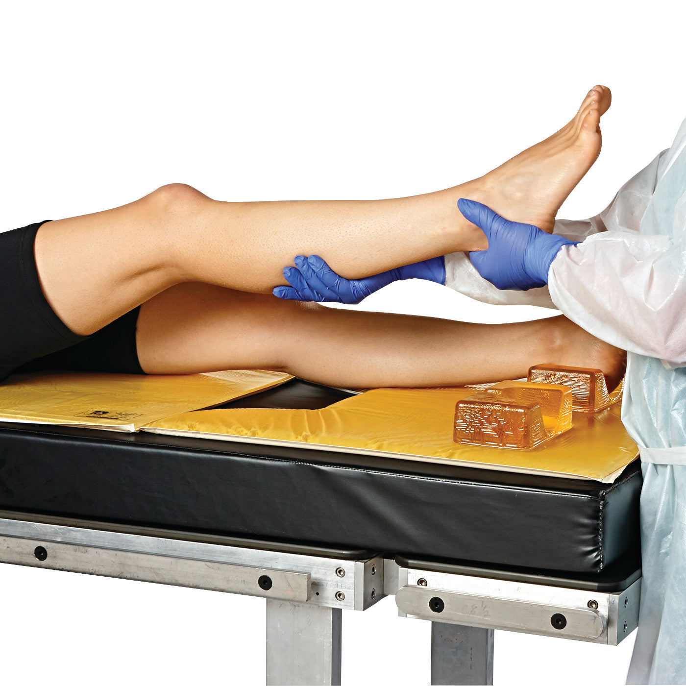 A person positions another's leg on a table using the AliMed AliGel Select Positioning Set, featuring yellow gel supports.