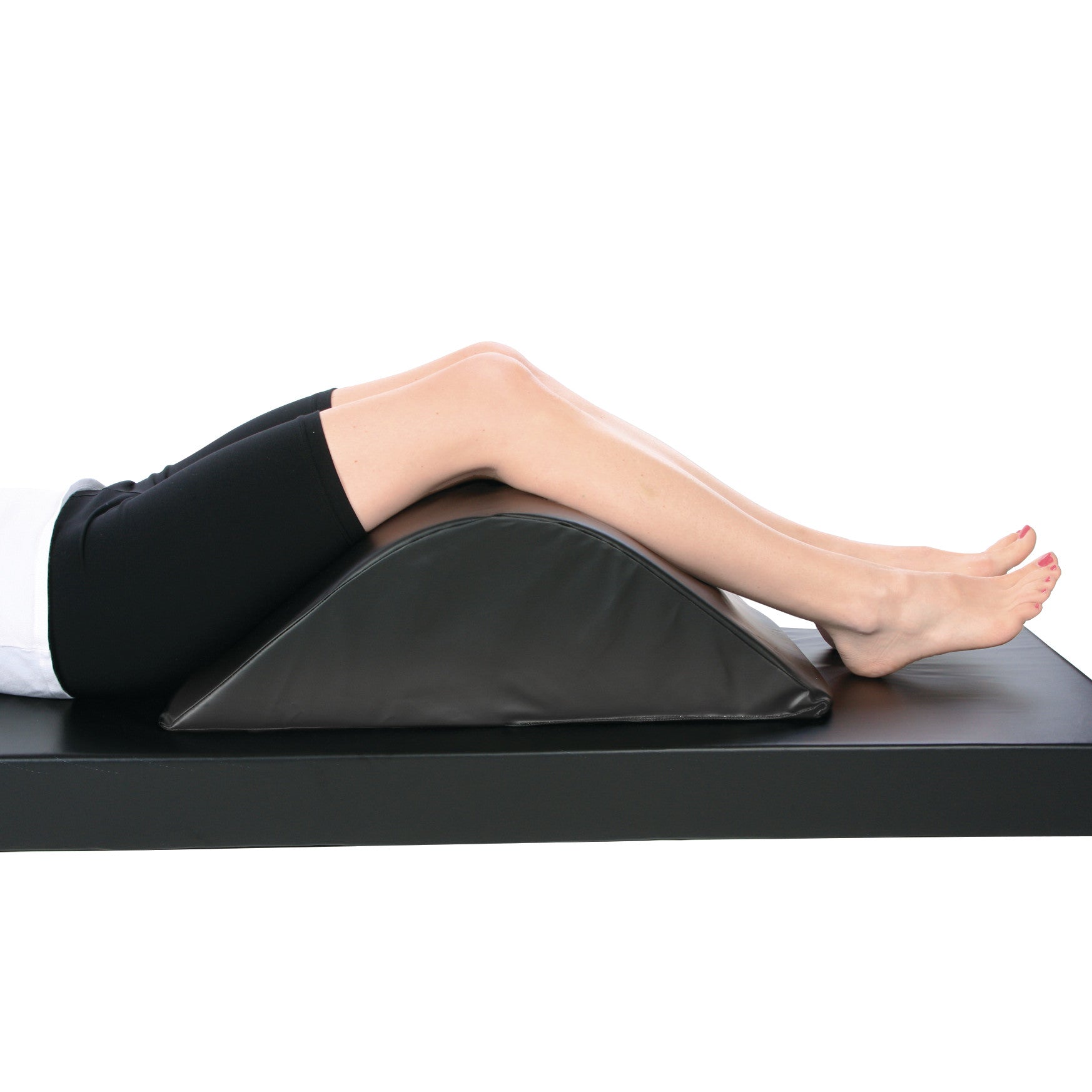 A person's legs are elevated on an AliMed Vinyl-Covered Deluxe Knee Bolster/Lumbar Positioner, providing support while lying down.