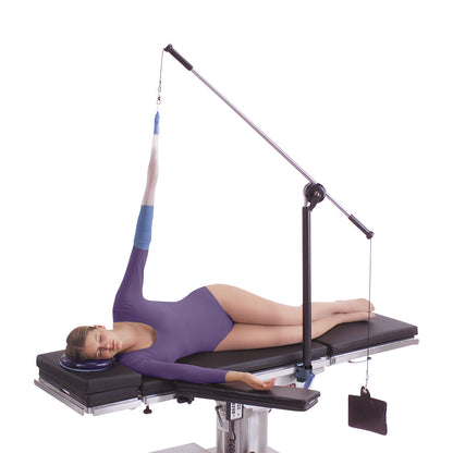 A person lies on a table with their arm secured in an elevated position using the Allen Arm Traction Device wearing a purple outfit.