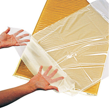 Hands holding a transparent AliMed Disposable Fitted Sheet Style Cover for Gel Surface Overlay on a yellowish cushion.