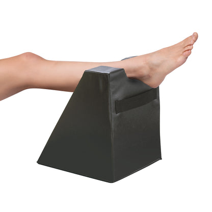 A foot rests on the AliMed High Foot Prepper, a black wedge-shaped cushion designed for elevating legs and feet.