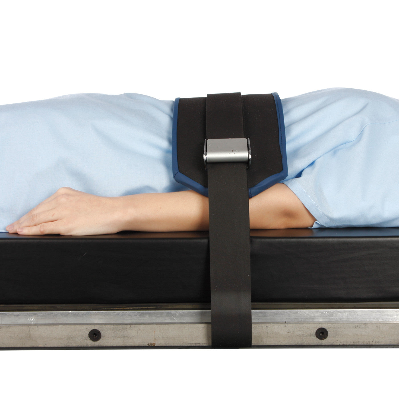 A person is secured with the AliMed Deluxe Padded O.R. Table Strap, lying on a black table with arms at their sides.