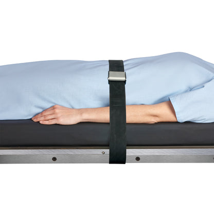 A person in a blue gown lies on a surface secured by an AliMed Economy Strap, featuring a black buckle, across their body.